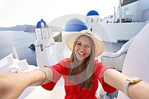 Excited traveler girl taking selfie photo in Santorini on sunset. Young woman having fun in Oia pictureque village in Greece