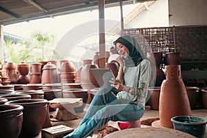 Excited veiled woman uses a tablet in a pottery shop