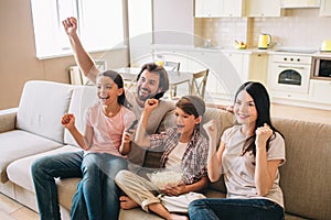 Excited and very happy family is rejoycing. They holds their fists up. Boy has bowl of popcorn. They look happy.