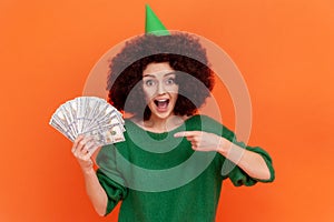 Excited woman with Afro hairstyle wearing green casual style sweater and party cone, having big sum