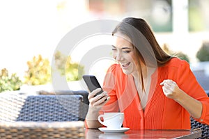 Excited woman checking smart phone content in a coffee shop