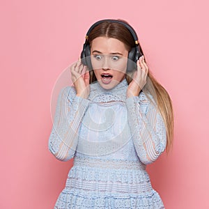 Excited woman dancing and listen to music wearing headphones in pink wall