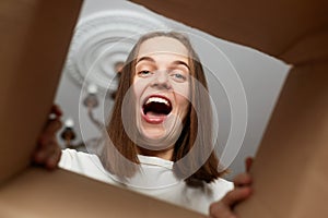 Excited woman with dark hair unpacking cardboard box, opening carton parcel and trying to get something, screaming with happiness