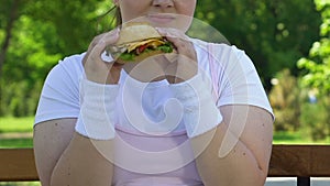 Excited woman eating burger with great pleasure, ignoring her diet, addiction