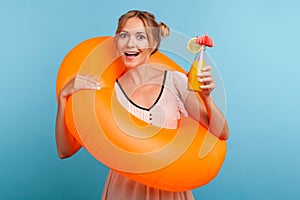 Excited woman with funny hair buns relaxing at summer resort, holding orange rubber ring and enjoying fresh fruit cocktail,