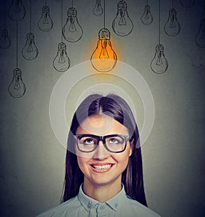 Excited woman in glasses looking up at bright light bulb above head has an idea