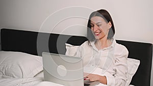 Excited woman has good news using laptop on bedroom. Smiling woman working on laptop. Joyful winner celebrating victory