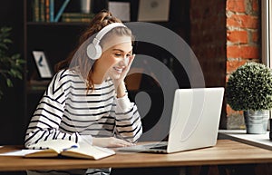 Excited woman in headphones having conversation on video chat while using laptop at home