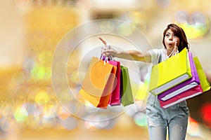 Excited woman holding colorful shopping bags pointing fingers on bokeh light soft effect background. Happiness,