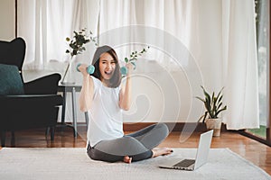 Excited woman holding dumbbells in both hand at home with laptop