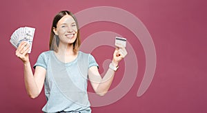 Excited woman holding money and credit card isolated over pink crimson background