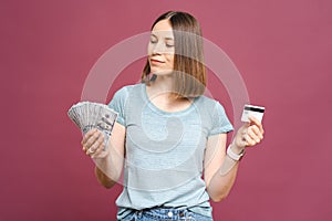 Excited woman holding money and credit card isolated over pink crimson background