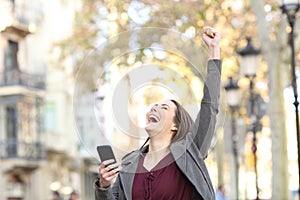 Excited woman holding phone and raising arm in the street