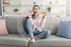 Excited woman holding remote control and debit credit card