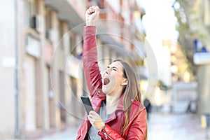 Excited woman holding smart phone celebrates success