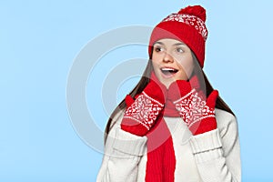 Excited woman looking sideways in excitement. Surprised christmas girl wearing knitted warm hat and scarf, isolated on blue