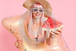 Excited woman with pink hair in swimsuit and sunglasses holding watermelon slice and inflatable star for swimming