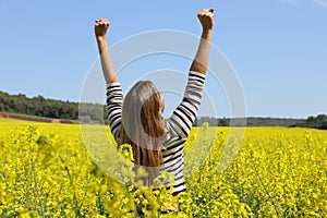 Excited woman raising arms in a field in summer vacation