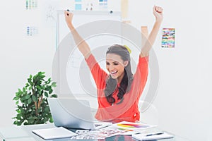 Excited woman raising her arms while working on her laptop