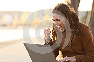 Excited woman reading good news on laptop in winter