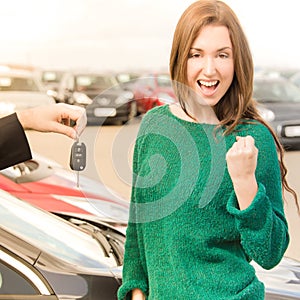 Excited woman receiving key in front of cars