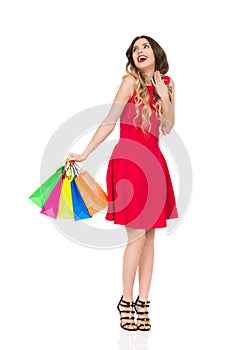 Excited Woman In Red Dress With Colorful Shopping Bags Is Smiling And Looking Up