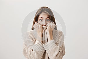 Excited woman trying to control emotions hearing shocking rumor. Emotive good-looking girl pulling sweater on face and