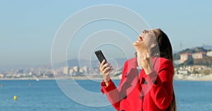 Excited woman using phone on the beach in winter