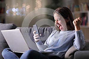 Excited woman using phone and laptop in the night