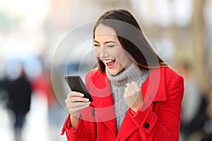 Excited woman using a smart phone in winter