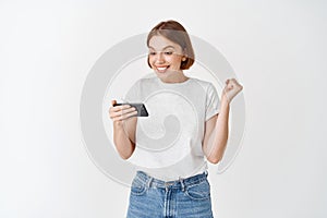 Excited woman winning video game on smartphone, looking happy at smartphone screen and say yes, fist pump to celebrate