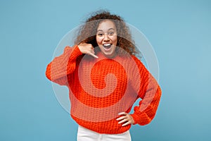Excited young african american girl in casual orange knitted clothes isolated on pastel blue background in studio