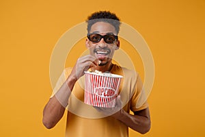 Excited young african american guy in 3d imax glasses posing isolated on yellow orange background in studio. People photo