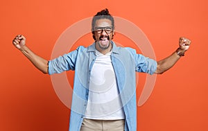 Excited young african american man winner raising arms with clenched fists and celebrating success