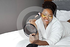 Excited young African woman with gold eye mask, medical eye antiwrinkle patches and doing natural nude make-up