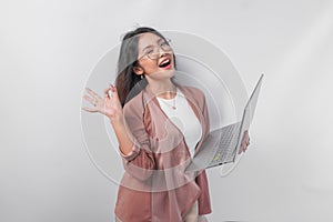 Excited young Asian business woman showing okay sign with right hand and holding laptop on isolated white background
