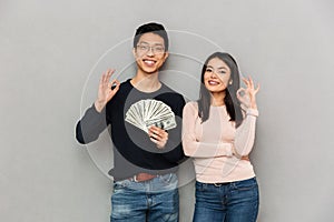 Excited young asian loving couple holding money showing okay gesture.