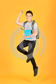 Excited young Asian man jumping with a backpack on the an orange background