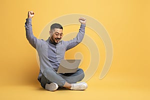 Excited Young Asian Man Using Laptop And Celebrating Success With Raised Hands