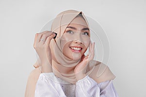 Excited young Asian Muslim woman wearing white dress and hijab testing or applying skin care serum on face. Facial and beauty