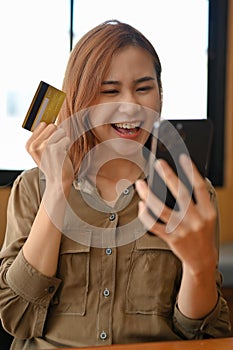 Excited young asian woman enjoy shopping on online website and paying with credit card