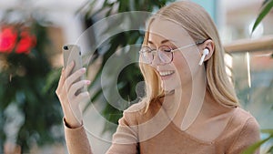 Excited young attractive millennial girl with wireless headset chat by video call use app on phone caucasian woman with