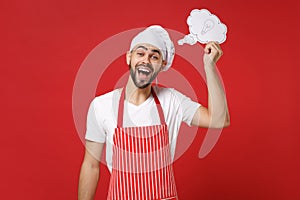 Excited young bearded male chef cook or baker man in striped apron toque chefs hat isolated on red background in studio