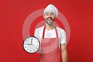 Excited young bearded male chef cook or baker man in striped apron white t-shirt toque chefs hat isolated on red