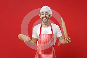 Excited young bearded male chef cook or baker man in striped apron white t-shirt toque chefs hat posing isolated on red