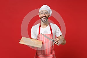 Excited young bearded male chef cook or baker man in striped apron white t-shirt toque chefs hat posing isolated on red