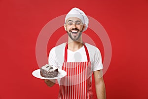 Excited young bearded male chef cook or baker man in striped apron white t-shirt toque chefs hat posing isolated on red