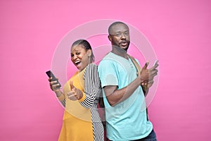 excited young black people standing back to back viewing contents on their phones, looking surprised, young african man and woman photo