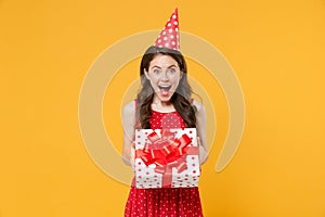 Excited young brunette woman girl in red summer dress, birthday hat posing isolated on yellow background. Birthday