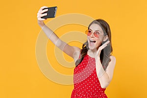 Excited young brunette woman girl in red summer dress, eyeglasses posing isolated on yellow background. People lifestyle